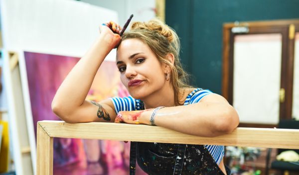Artiste en atelier semblant réfléchir face à son travail, illustrant les doutes et blocages liés à la visibilité